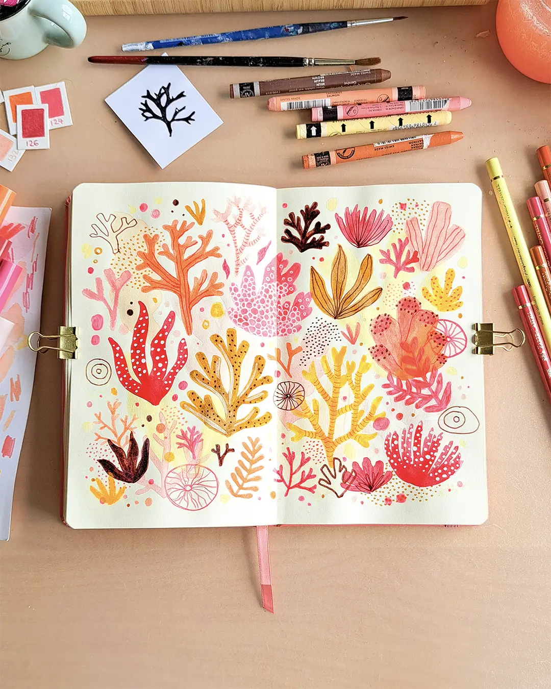 Page de carnet de croquis avec des illustrations d'algues et de coraux, dans des couleurs chaudes.