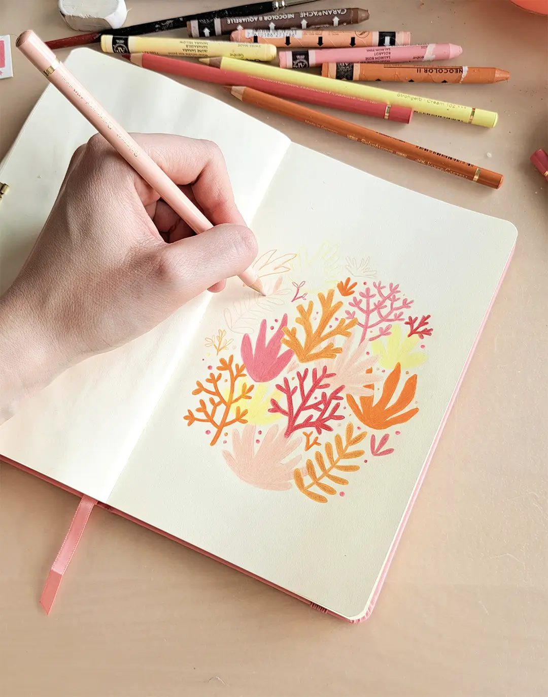 Illustratrice en train de dessiner des algues et des coraux sur une page de carnet de croquis.